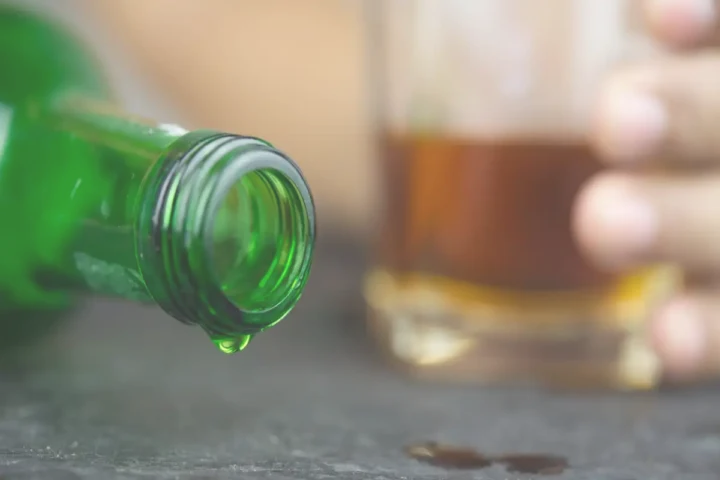 green bottle dripping liquid beside glass on table