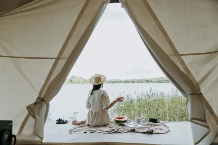 woman relaxing inside tent overlooking lake with picnic setup