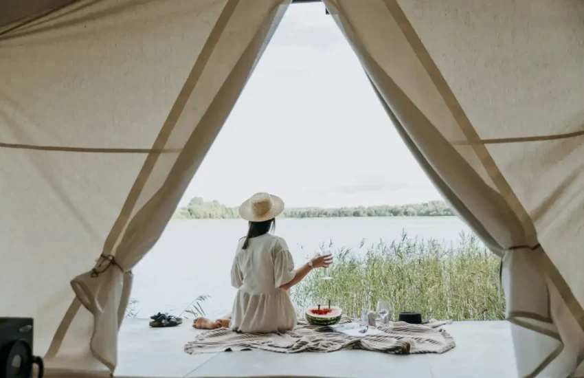 woman relaxing inside tent overlooking lake with picnic setup