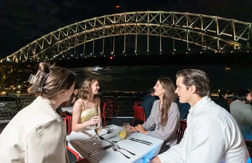 Guests enjoying dinner on a Sydney Harbour cruise with the illuminated Sydney Harbour Bridge in the background